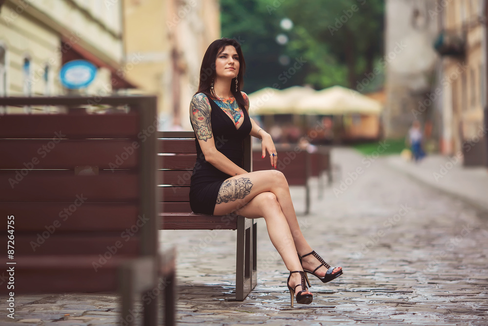 beautiful girl in a black dress sitting on a bench, covered in t