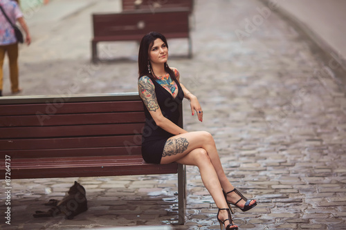 beautiful girl in a black dress sitting on a bench, covered in t photo