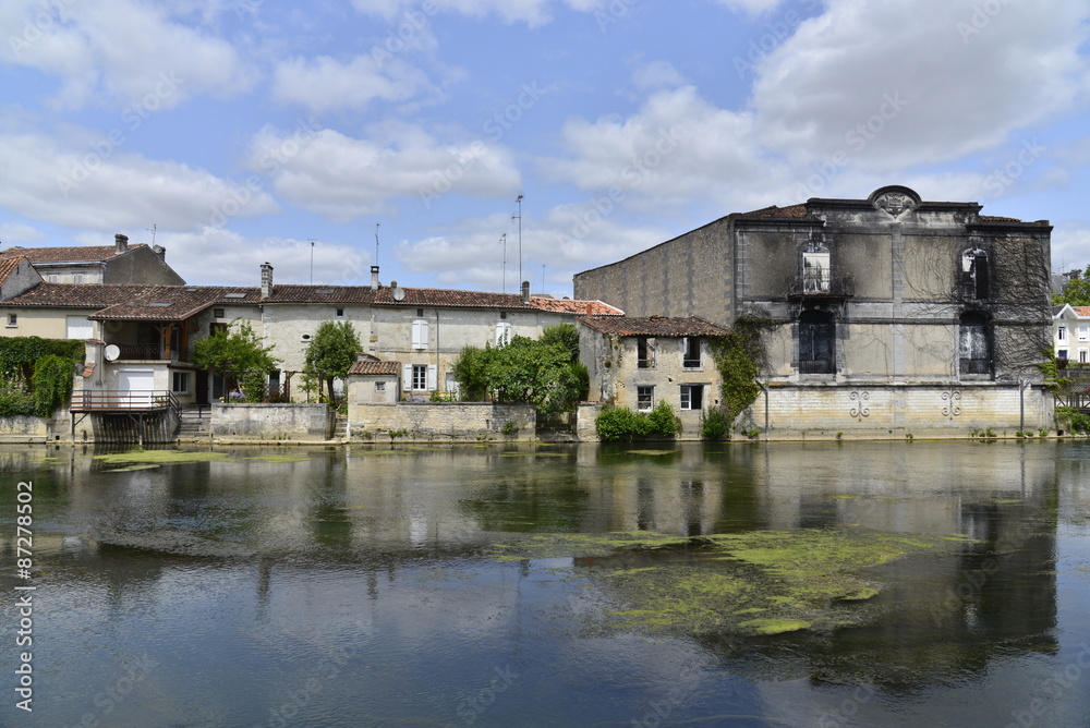 Un grand bâtiment gris et désaffecté à côté des maisons typiques au bord de la Charente