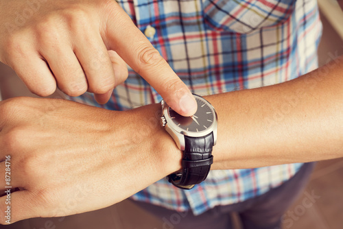 young man tapping his finger on his wristwatch