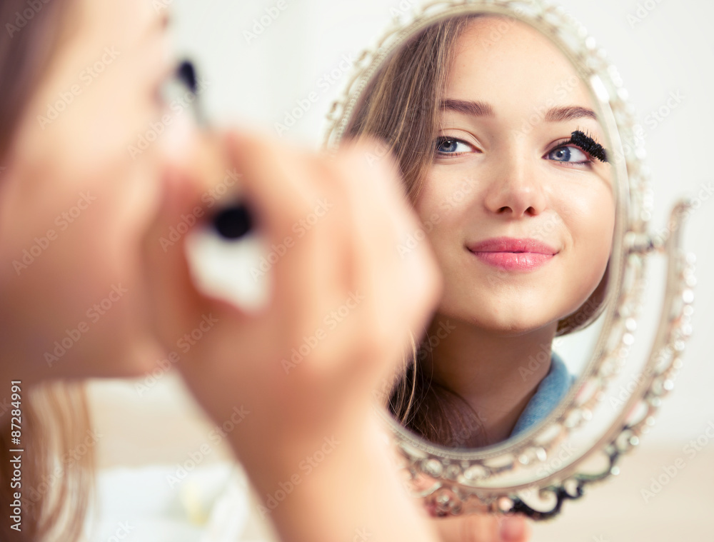 Beauty model teenage girl looking in the mirror and applying mascara Beauty model teenage girl looking in the mirror and applying mascara