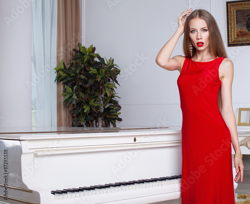 young gorgeous caucasia nblond in red dress on the chair, near white piano, studio shot photo