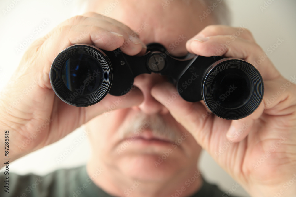 A senior man holds an old pair of binoculars pointed at the camera. A senior man holds an old pair of binoculars pointed at the camera.