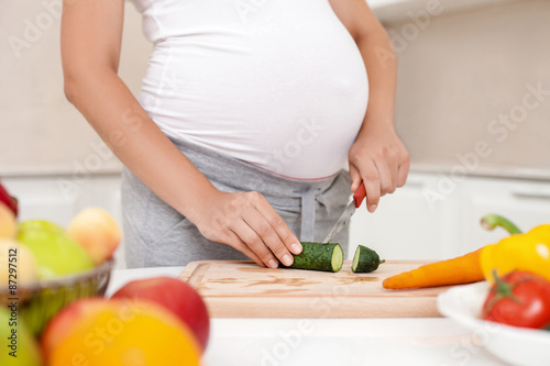 Young pregnant woman is making a salad in kitchen