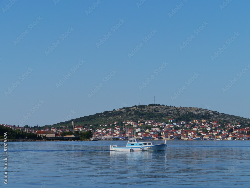The village Murter on the island Murter in the Adriatic sea of Croatia with a blue and white fishing boat in front The village Murter on the island Murter in the Adriatic sea of Croatia with a blue and white fishing boat in front