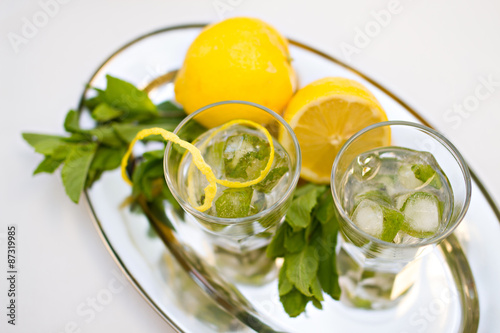 Two cocktail glasses and mint with lemons on tray