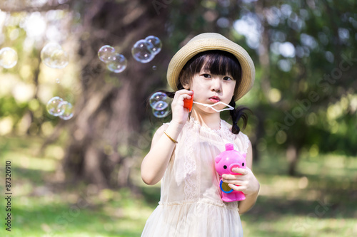 Asian little girl is blowing a soap bubbles with smile face in p