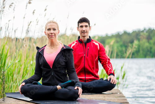 Paar macht Yoga auf Steg am See, Frau und Mann beim Meditieren