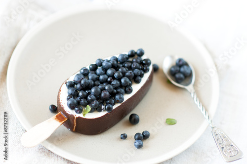 Ice cream with chocolate glaze on plate garnished with fresh blueberries.