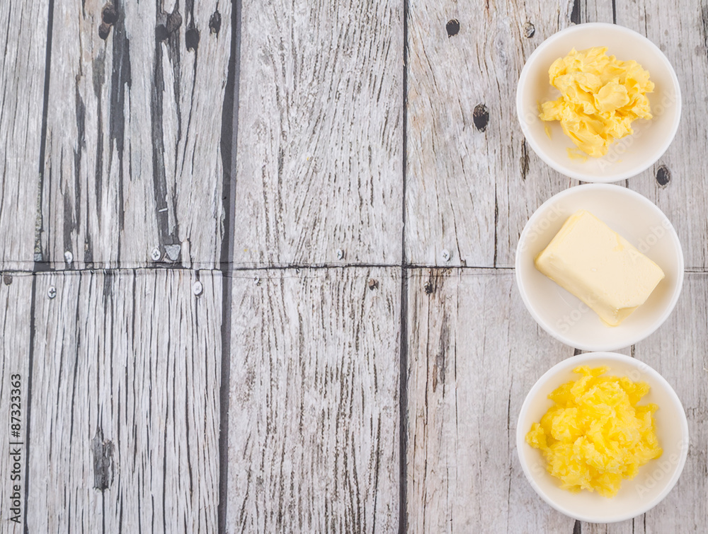 A block of butter, margarine and ghee in white bowls over rustic wooden background A block of butter, margarine and ghee in white bowls over rustic wooden background
