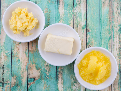Tablou pe pânză A block of butter, margarine and ghee in white bowls over rustic wooden backgrou