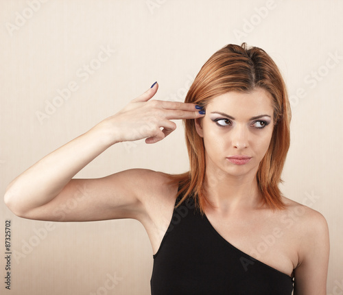Beautiful young woman holding her finger against her head.