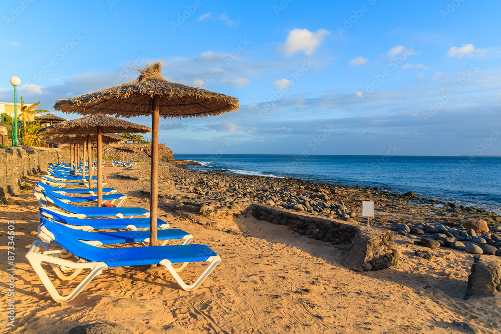 Row of sunbeds and umbrellas on Playa Blanca beach at sunset time, Lanzarote, Canary Islands, Spain