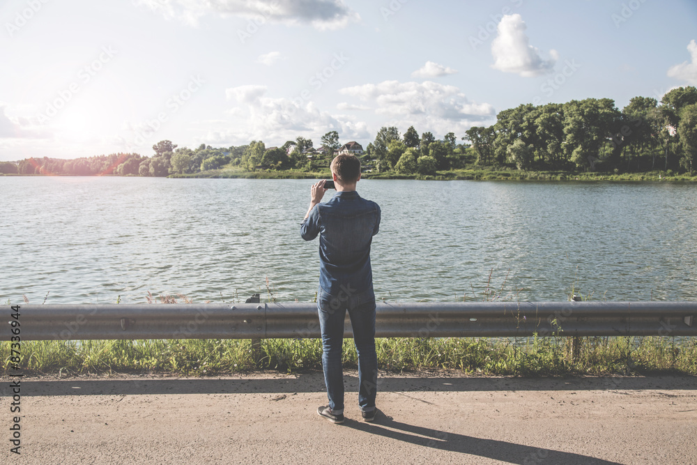 Man standing in front of the lake and the photographs on the smartphone Man standing in front of the lake and the photographs on the smartphone