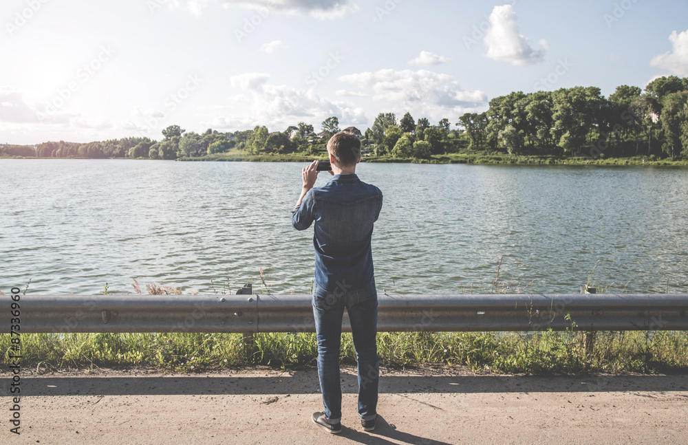 Man standing in front of the lake and the photographs on the smartphone Man standing in front of the lake and the photographs on the smartphone