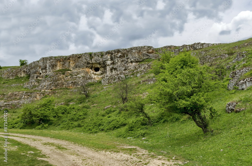 General view toward sedimentary rock with cave in the field, Ludogorie, Bulgaria