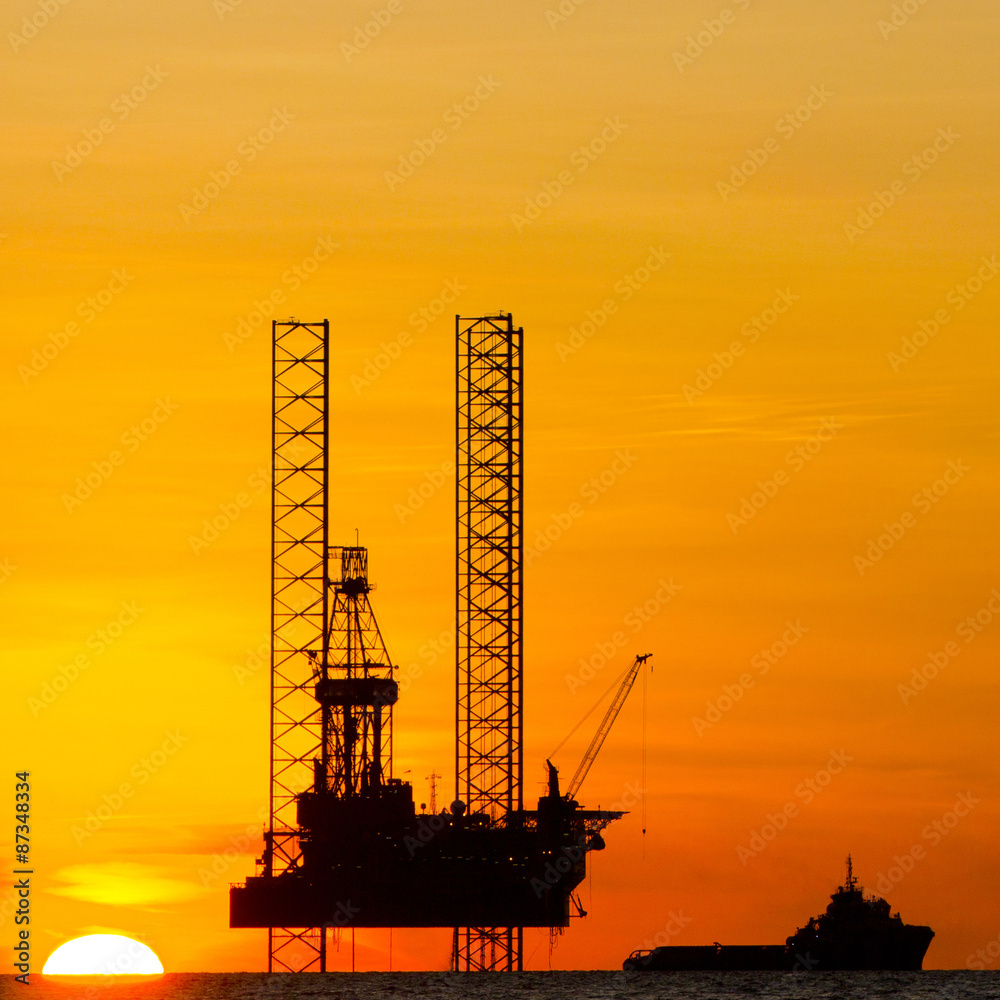 Silhouette of an offshore drilling rig and supply vessel at sunset