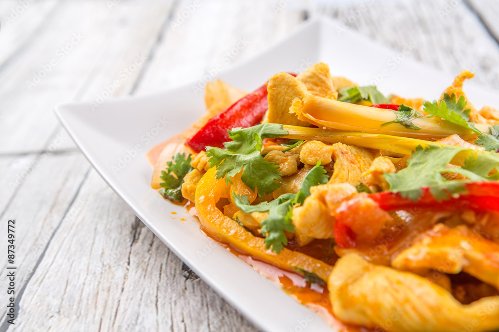 Malaysian traditional dish of Ayam Paprik or spicy stir fry chicken on white plate over wooden background Malaysian traditional dish of Ayam Paprik or spicy stir fry chicken on white plate over wooden background