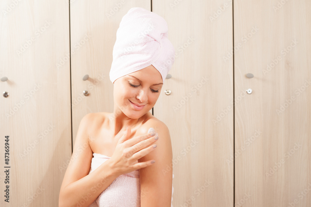 Young woman applying skin cream after shower in gym Young woman applying skin cream after shower in gym