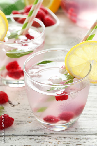 Raspberries and juice in glass on white wooden background