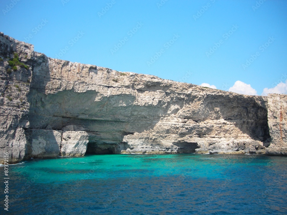 Rocky coast and transparent, cyan waters of the Blue Lagoon on the island of Comino, Malta, on a sunny summer day.