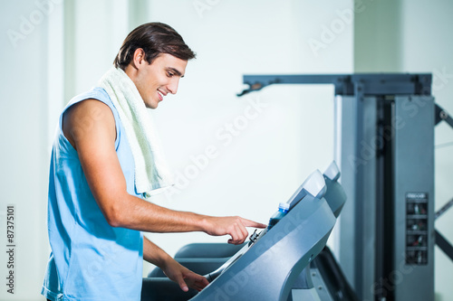 Happy man adjusts treadmill in gym