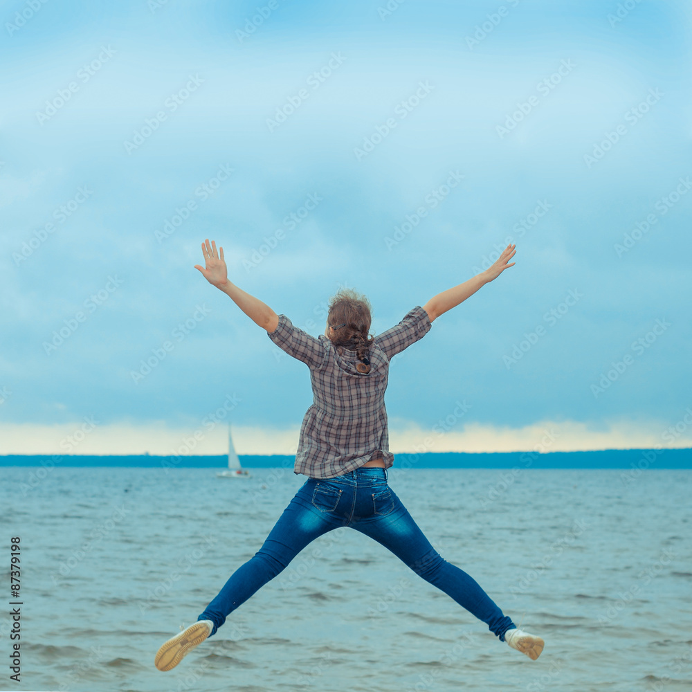 cheerful teen girl jumping on the beach in cloudy windy weather