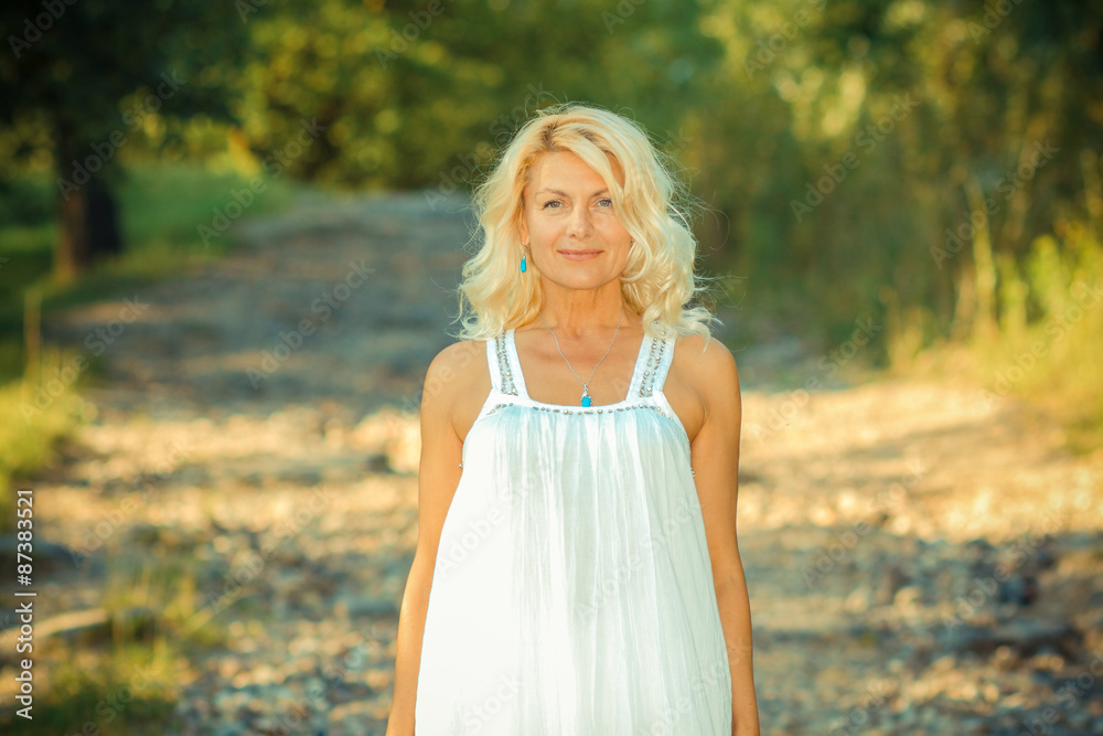 romantic portrait of a beautiful older woman. Mature beautiful blonde in a white dress walks on the road romantic portrait of a beautiful older woman. Mature beautiful blonde in a white dress walks on the road