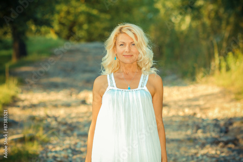 romantic portrait of a beautiful older woman. Mature beautiful blonde in a white dress walks on the  road