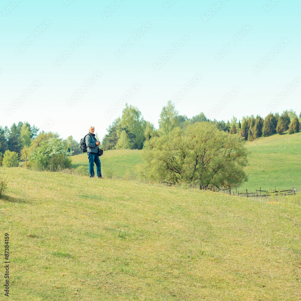 Elderly man travels in wildlife. Portrait of the gray-haired traveler in background of the landscape. Old photographer enjoys traveling and photography Elderly man travels in wildlife. Portrait of the gray-haired traveler in background of the landscape. Old photographer enjoys traveling and photography