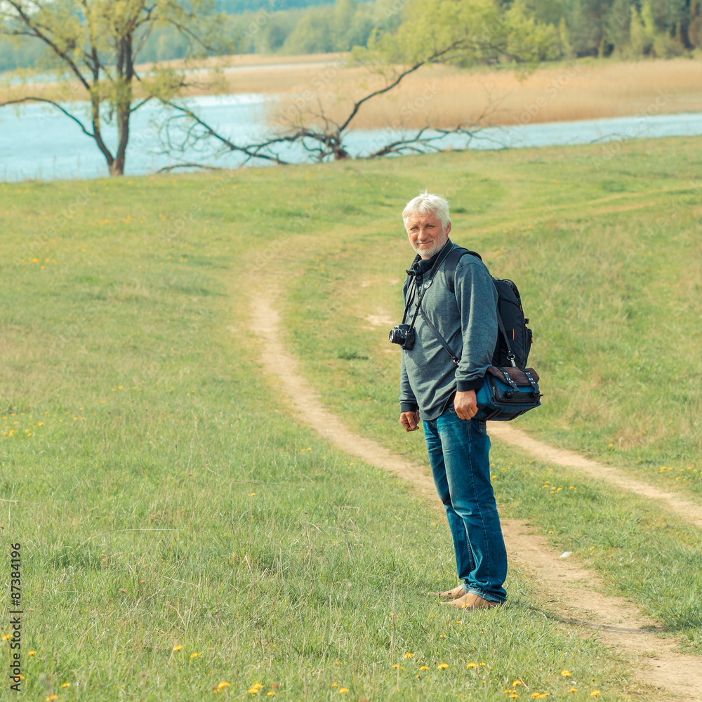 Elderly man travels in wildlife. Portrait of the gray-haired traveler in background of the landscape. Old photographer enjoys traveling and photography Elderly man travels in wildlife. Portrait of the gray-haired traveler in background of the landscape. Old photographer enjoys traveling and photography