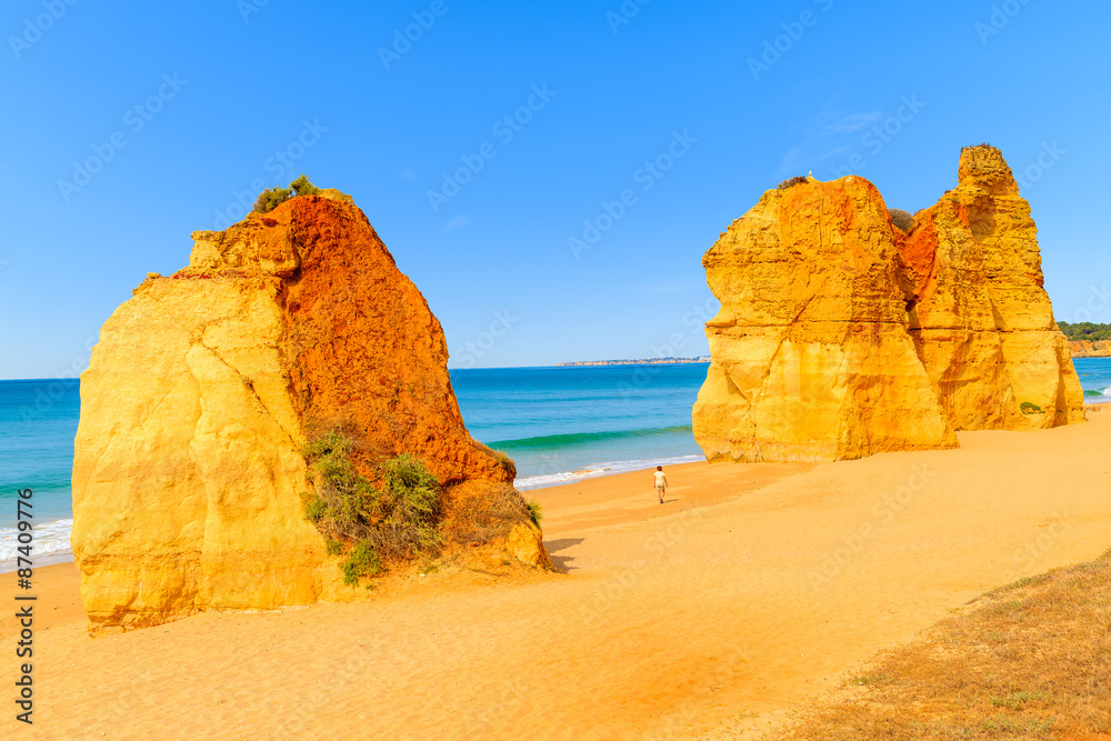 Tourist walking between rocks on beautiful Praia da Rocha beach, Algarve region, Portugal