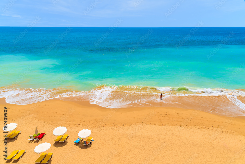 Sun umbrellas and young woman in sea on beautiful Praia da Rocha beach, Algarve region, Portugal