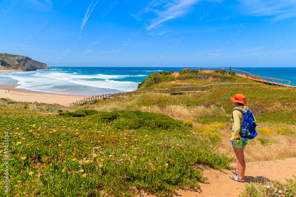 Young woman tourist on walking path to Praia do Amado beach in spring, Algarve region, Portugal