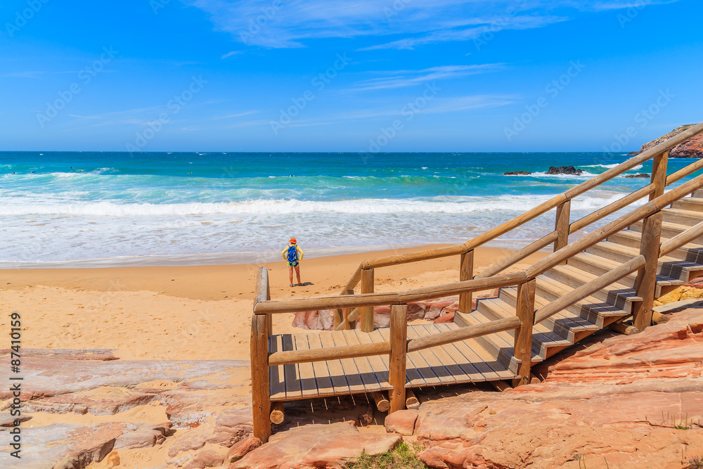 Walkway to Praia do Amado beach and young woman tourist standing in distance, Algarve region, Portugal