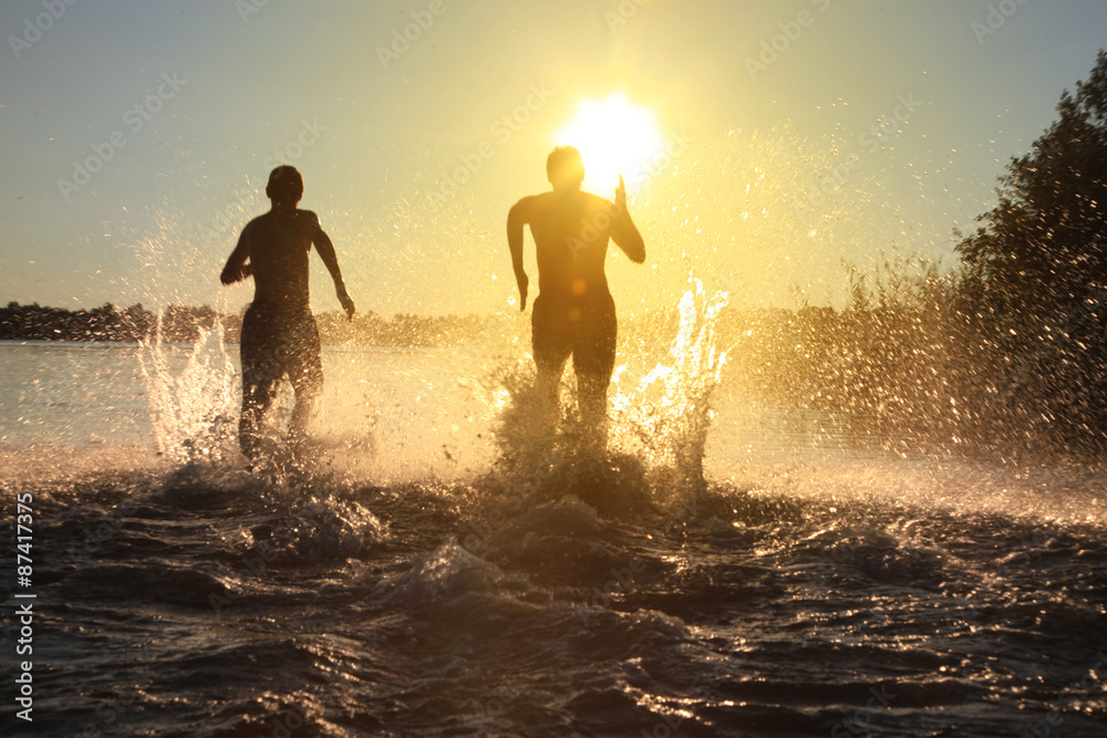 Fototapeta premium Glückliche junge Menschen laufen und springen am See beim Sonnenuntergang