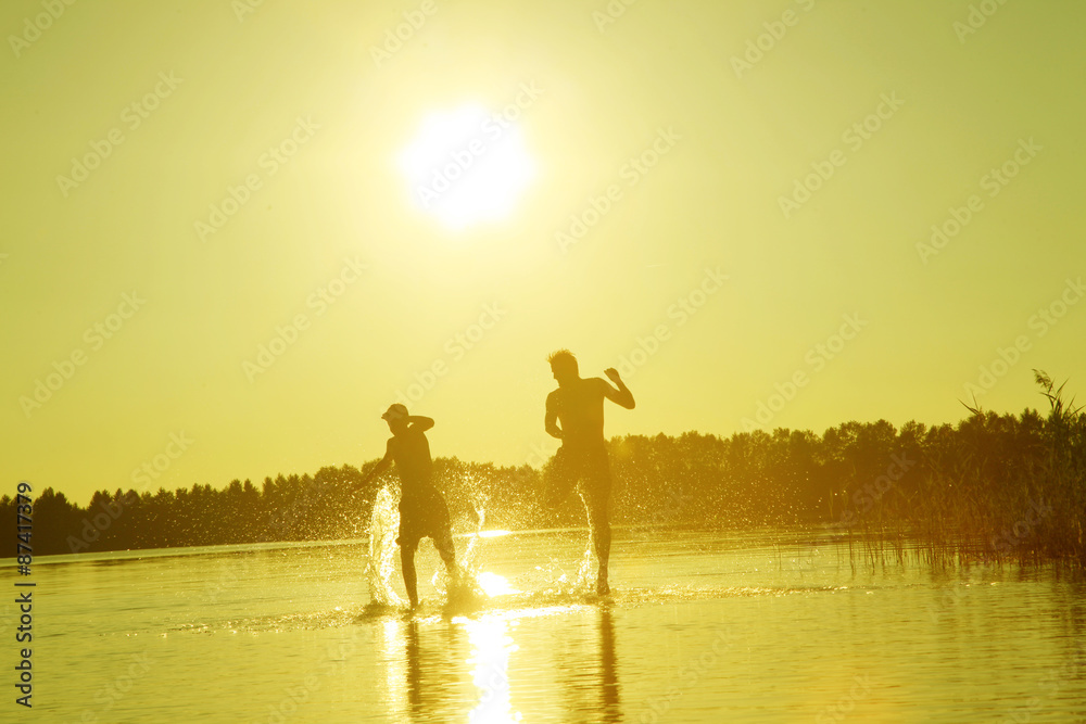 Fototapeta premium Glückliche junge Menschen laufen und springen am See beim Sonnenuntergang