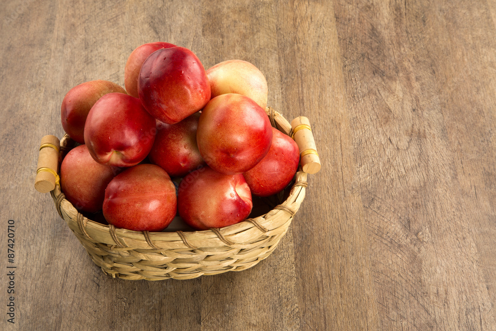 Some peaches in a basket over a wooden surface on a green and na Some peaches in a basket over a wooden surface on a green and na