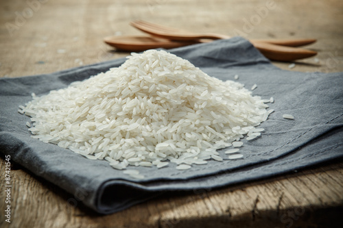 Uncooked rice grains on the fabric with wooden spoon and folk -