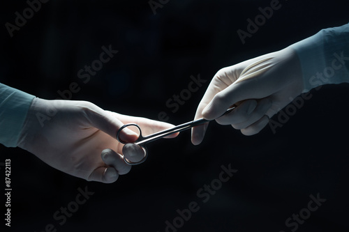 healthcare and medical concept , Close-up of surgeons hands holding surgical scissors and passing surgical equipment on black