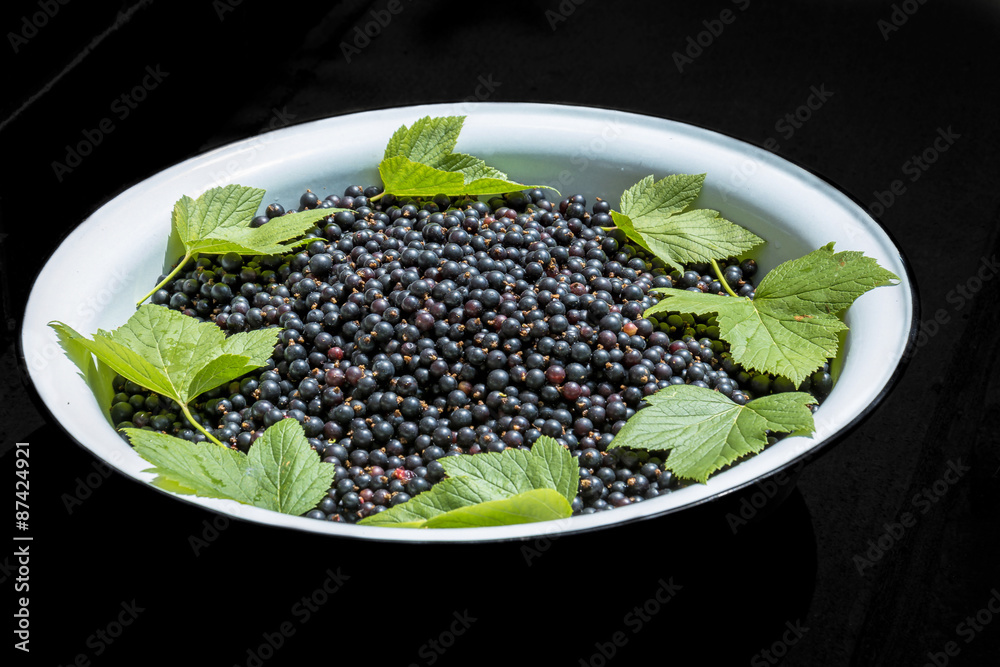 Currant in bowl with currant leaves on black background Currant in bowl with currant leaves on black background