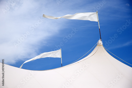Marquee roof with flags blowing in the wind against a blue sky