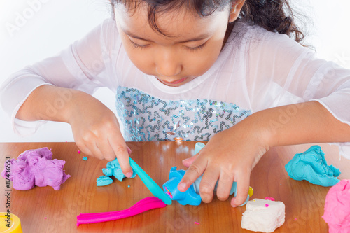 Little girl is learning to use colorful play dough on white background
