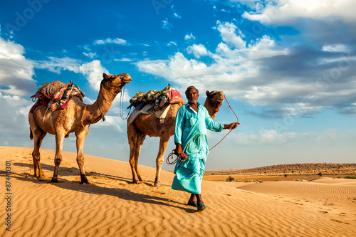 Fotografie Cameleer camel driver with camels in dunes of Thar desert