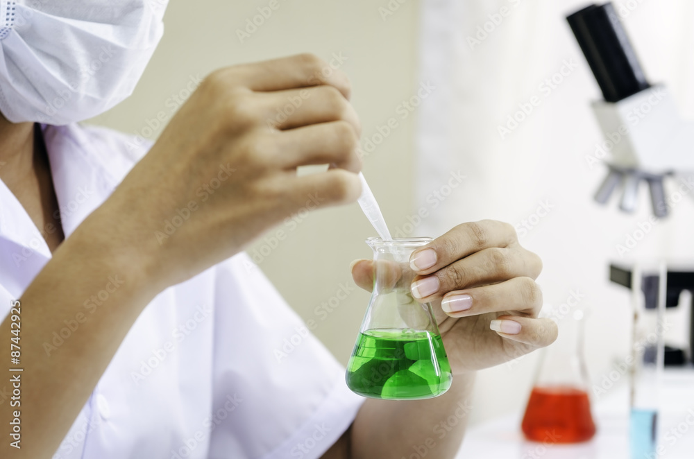 researcher’s hand dropping a green liquid in a beaker researcher’s hand dropping a green liquid in a beaker