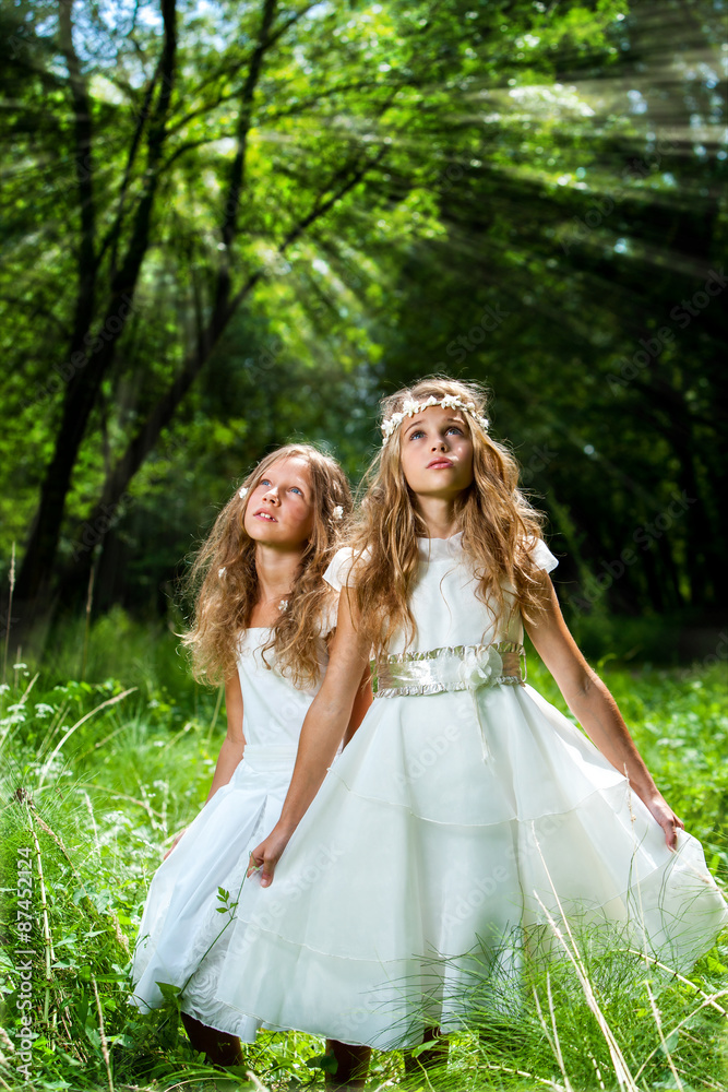 Litte princesses wearing white dresses in woods.