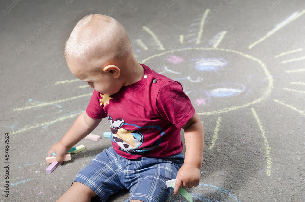 Naklejka premium little boy draws with chalk on the pavement sun
