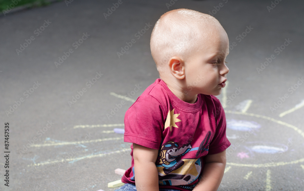 Naklejka premium little boy draws with chalk on the pavement sun