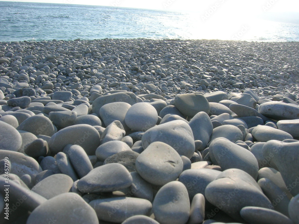 Obraz premium Closeup of white pebbles on the beach on a late sunny afternoon, low angle perspective.