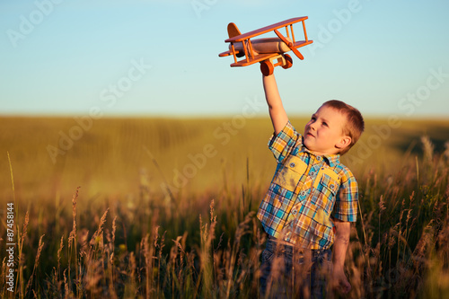 small boy playing with plane on meadow